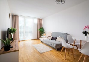 Ein modernes Wohnzimmer mit einer Couch, Sesseln, einem kleinen Tisch und Topfpflanzen.