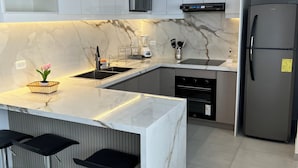 A modern kitchen with white cabinets, a marble countertop, a built-in microwave, a stainless steel refrigerator, and a bar area with stools. - Delightful 3-bedroom apartment in Tumbaco, Quito (Quito)