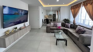 A modern living room with a flat-screen TV, a sofa set, a glass coffee table, and a kitchen in the background. - Delightful 3-bedroom apartment in Tumbaco, Quito (Quito)