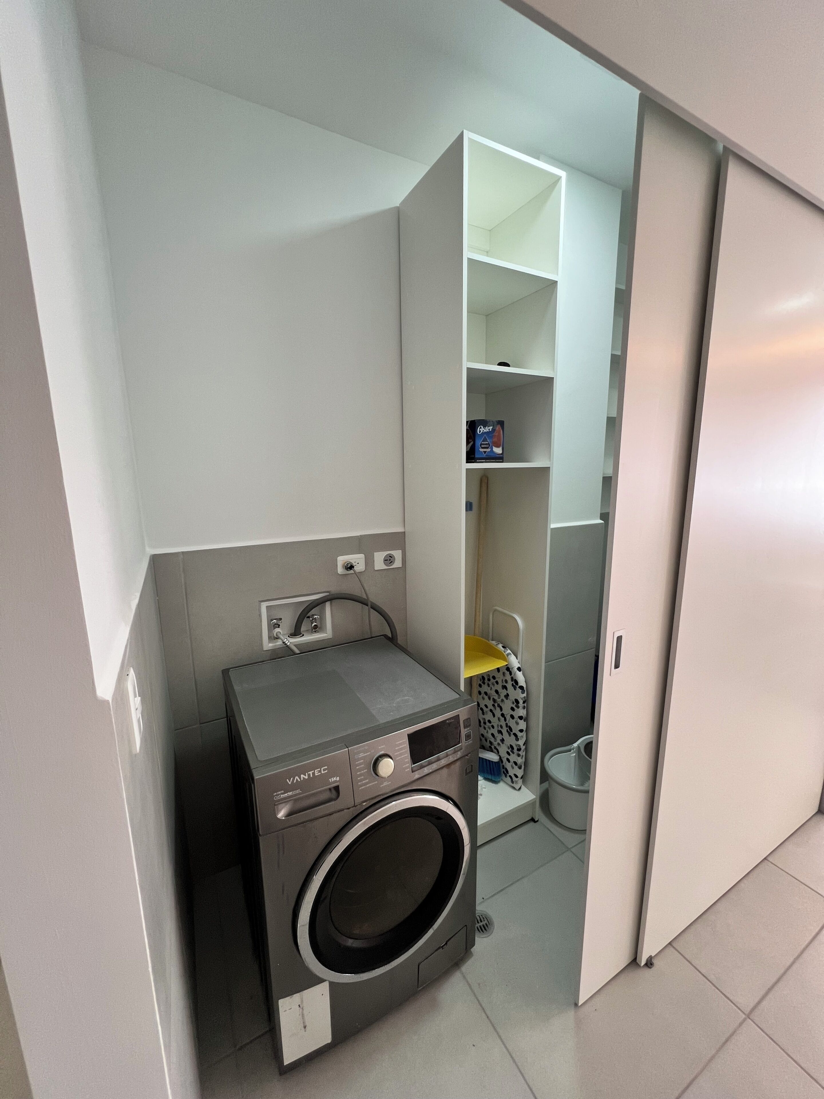 Ein kleiner Hauswirtschaftsraum mit einer Waschmaschine mit Frontlader, einem Regal mit Waschmittel und einer Toilette.