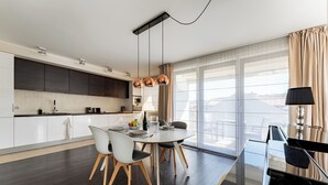 A modern kitchen with dark cabinets, a dining area with a round table and chairs, and large windows with curtains.