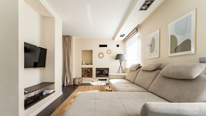 A modern living room with a large sectional sofa, a flat-screen TV mounted on the wall, a fireplace, and a floor lamp.