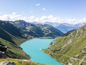 Eine Berglandschaft mit einem türkisblauen See, umgeben von grünen Hügeln und fernen Bergen.