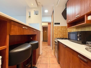 A kitchen with wooden cabinets, a black countertop, a microwave, and a stove. - Wrocław Skyline Apartment (Wrocław)
