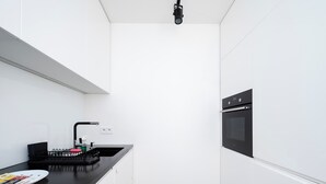 A modern kitchen with white cabinets, a black countertop, a built-in oven, and a black faucet.
