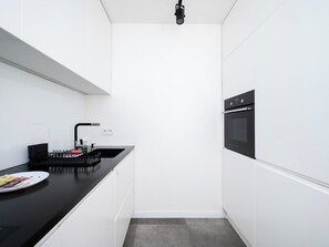 Una cocina moderna con gabinetes blancos, encimera negra, horno empotrado y grifo negro.