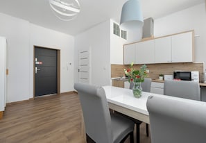 Eine moderne Küche mit weißen Schränken, einer Mikrowelle und einem Essbereich mit weißem Tisch und grauen Stühlen.