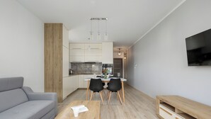 A modern living space with a grey sofa, wooden coffee table, dining area with chairs, and a TV mounted on the wall. - Raginisa Superior Apartment (Szczecin)