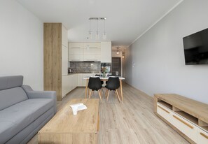 Ein modernes Wohnzimmer mit grauem Sofa, Holz-Couchtisch, Essbereich mit Stühlen und einem an der Wand befestigten Fernseher.