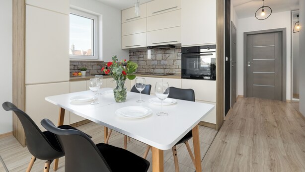 A modern kitchen with white cabinets, a stone backsplash, and a dining table set with plates and glasses. - Raginisa Superior Apartment (Szczecin)