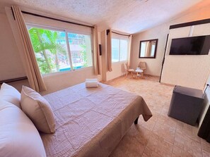 Une chambre d’hôtel avec un lit, une petite table, une chaise, un téléviseur et une fenêtre avec des rideaux.