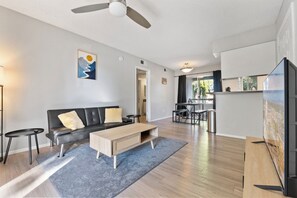 A modern living room with a sofa, coffee table, and TV, leading to a kitchen and dining area.