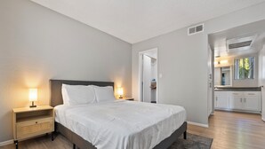 Une chambre à coucher moderne, avec un lit, des tables de chevet et une vue sur la cuisine.