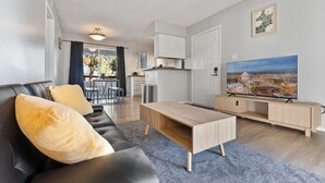 Un salon moderne avec un canapé en cuir noir, une table basse en bois et un téléviseur posé sur un meuble en bois.