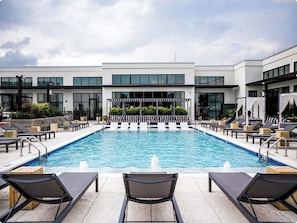 A modern hotel with a rectangular swimming pool surrounded by lounge chairs and a covered seating area.