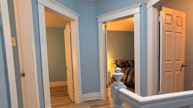 A hallway with wooden flooring, white walls, and a white railing.