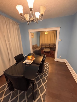 A dining area with a black table, chairs, and a chandelier. There is a living room in the background with a sofa and a coffee table. - Two story House: 3 Bed room 1/5 Bathroom (Winnipeg)