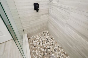 Ducha con piso de piedras y dispensador de jabón negro.