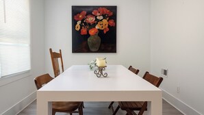 A dining room with a white table, six wooden chairs, and a painting of flowers on the wall. - Detroit 4BR Home | Bathtub and Pet Friendly Stay (Detroit)