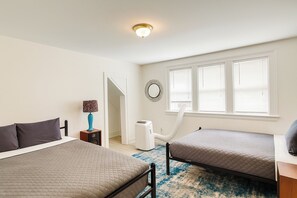 A bedroom with two beds, a nightstand, a lamp, a heater, and a window with blinds. - Detroit 4BR Home | Bathtub and Pet Friendly Stay (Detroit)