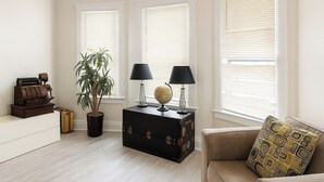A living room with a light wooden floor, a beige sofa with patterned cushions, a small black side table with a globe and lamps, a potted plant, and a vintage typewriter. - Detroit 4BR Home | Bathtub and Pet Friendly Stay (Detroit)