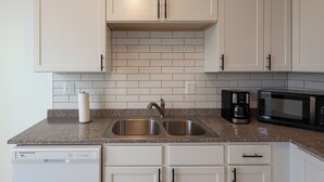 A kitchen with white cabinets, a granite countertop, a double sink, a coffee maker, and a microwave. - Detroit 4BR Home | Bathtub and Pet Friendly Stay (Detroit)