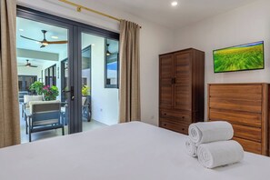 Ein Hotelzimmer mit Bett, Holzschrank, Fernseher und einer Glasschiebetür, die auf einen Balkon führt.