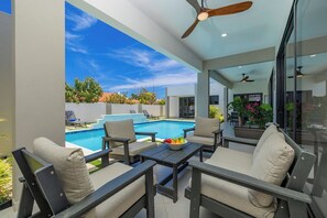 Eine Außenpatio mit Pool, Sitzgelegenheiten, Deckenventilatoren und Blick auf den Himmel.