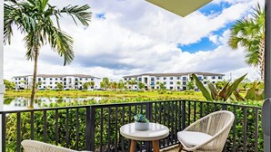 A balcony with wicker chairs, a small round table, and a view of a building across a pond.