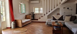 Ein Wohnzimmer mit einer Couch, einer hölzernen Bank, einem Tisch mit Büchern, einer Treppe und einem Fenster mit grünem Rollo.