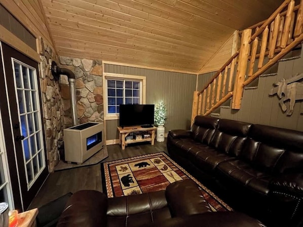 A cozy living room with a stone wall, a fireplace, a leather sofa, and a TV.