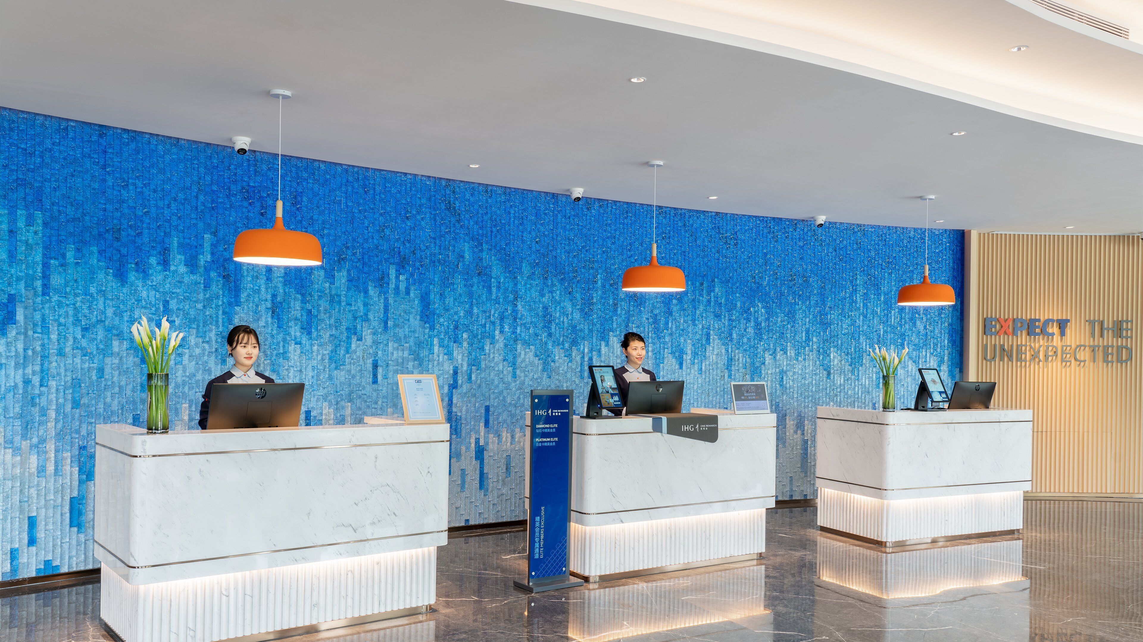 A reception area with two reception desks, blue mosaic wall, and a sign that reads "EXPECT THE UNEXPECTED".
