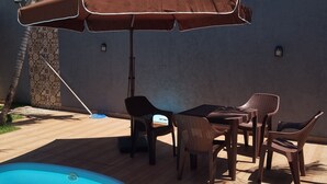 Ein Poolbereich mit Tisch und Stühlen, einem braunen Sonnenschirm und einem blauen Pool.