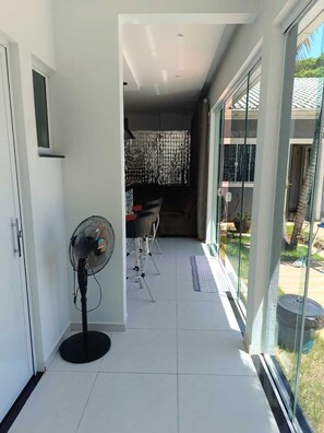 A hallway with a fan, a dining area with chairs and a table, and a view of the outside through large windows.