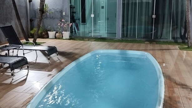 Ein Swimmingpool mit weißem Sonnenschirm, Liegestühlen und einer Glastür zu einem überdachten Bereich.