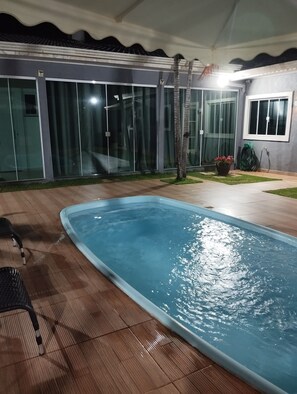 An outdoor swimming pool with a tiled deck, glass doors, and a small window.