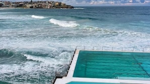 Ein Pool mit klarem Wasser, Blick auf den Ozean und eine entfernte Küste mit Gebäuden.