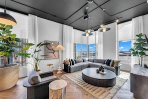 Ein modernes Wohnzimmer mit Ecksofa, rundem Couchtisch und großen Fenstern mit Blick auf die Stadt.
