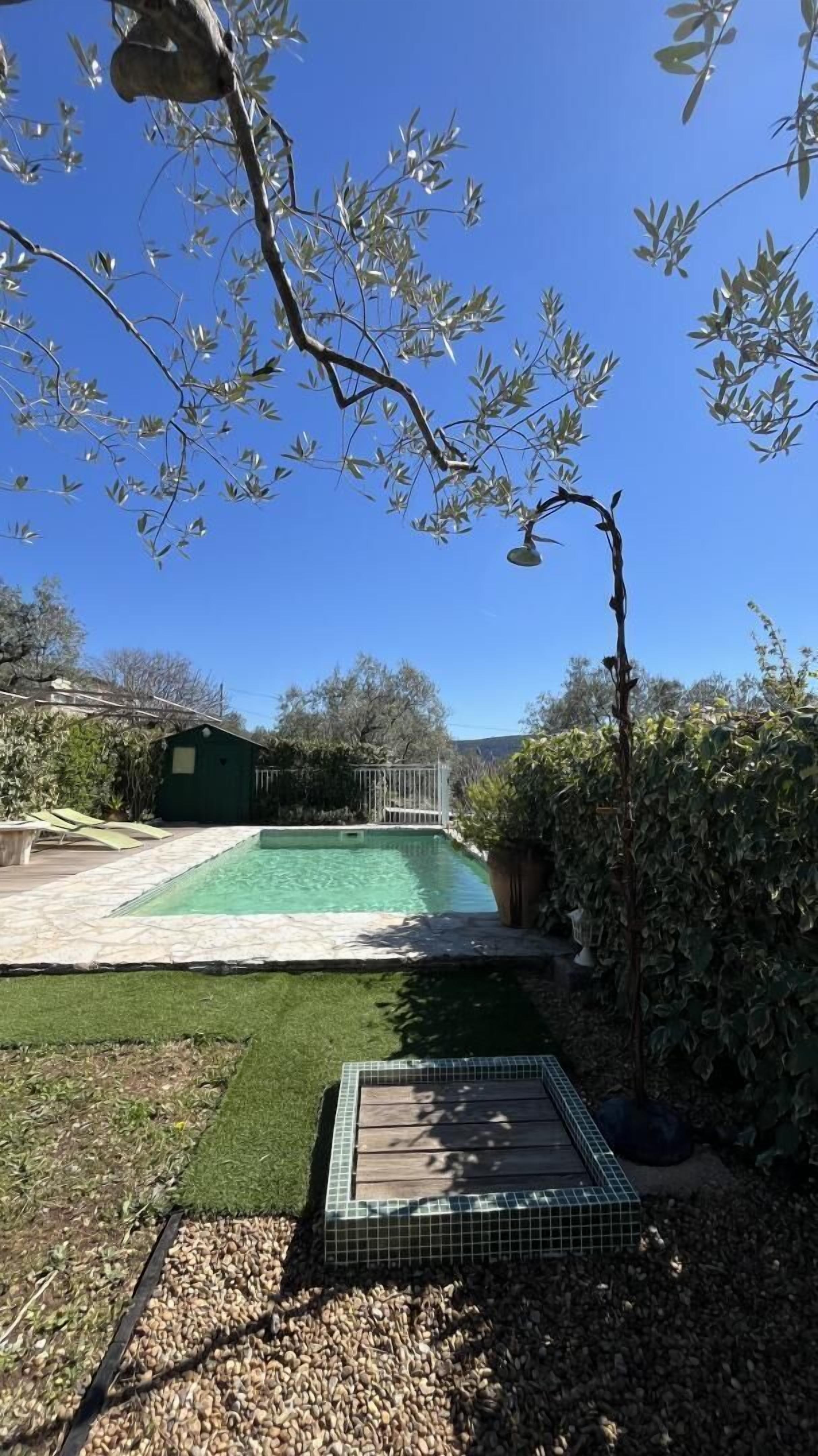 Un patio trasero con piscina, una pequeña terraza y un cobertizo verde.