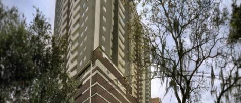 A high-rise building with a modern architectural design, surrounded by greenery and a clear sky.