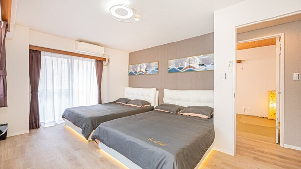 Et moderne hotelværelse med to senge, et stort vindue med gardiner, billedkunst på væggen og en aircondition-enhed.