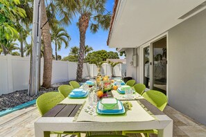 Un comedor al aire libre con una mesa dispuesta para seis personas, rodeado de palmeras y una cerca blanca.