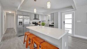 A modern kitchen with a large island, stainless steel appliances, and wooden bar stools. - Heated Pool Complimentary - Mini - Golf - Bicycles - Just 6 Minutes to the Beach (Fort Lauderdale)