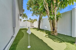 Spazio ristretto e recintato con erba sintetica, un bastoncino da golf e un albero con radici a vista.
