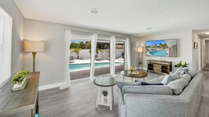 A modern living room with a pool view, a sofa, a TV, and a lamp. - Heated Pool Complimentary - Mini - Golf - Bicycles - Just 6 Minutes to the Beach (Fort Lauderdale)
