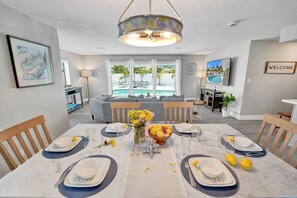 Comedor con mesa para cuatro, sofá al fondo y vista a la piscina.