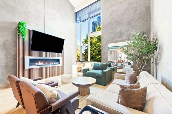 A modern living room with a fireplace, comfortable seating, and a large window offering a view of the city.