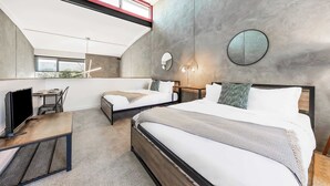 A modern hotel room with a loft-style ceiling, two beds, a desk, and a large window.