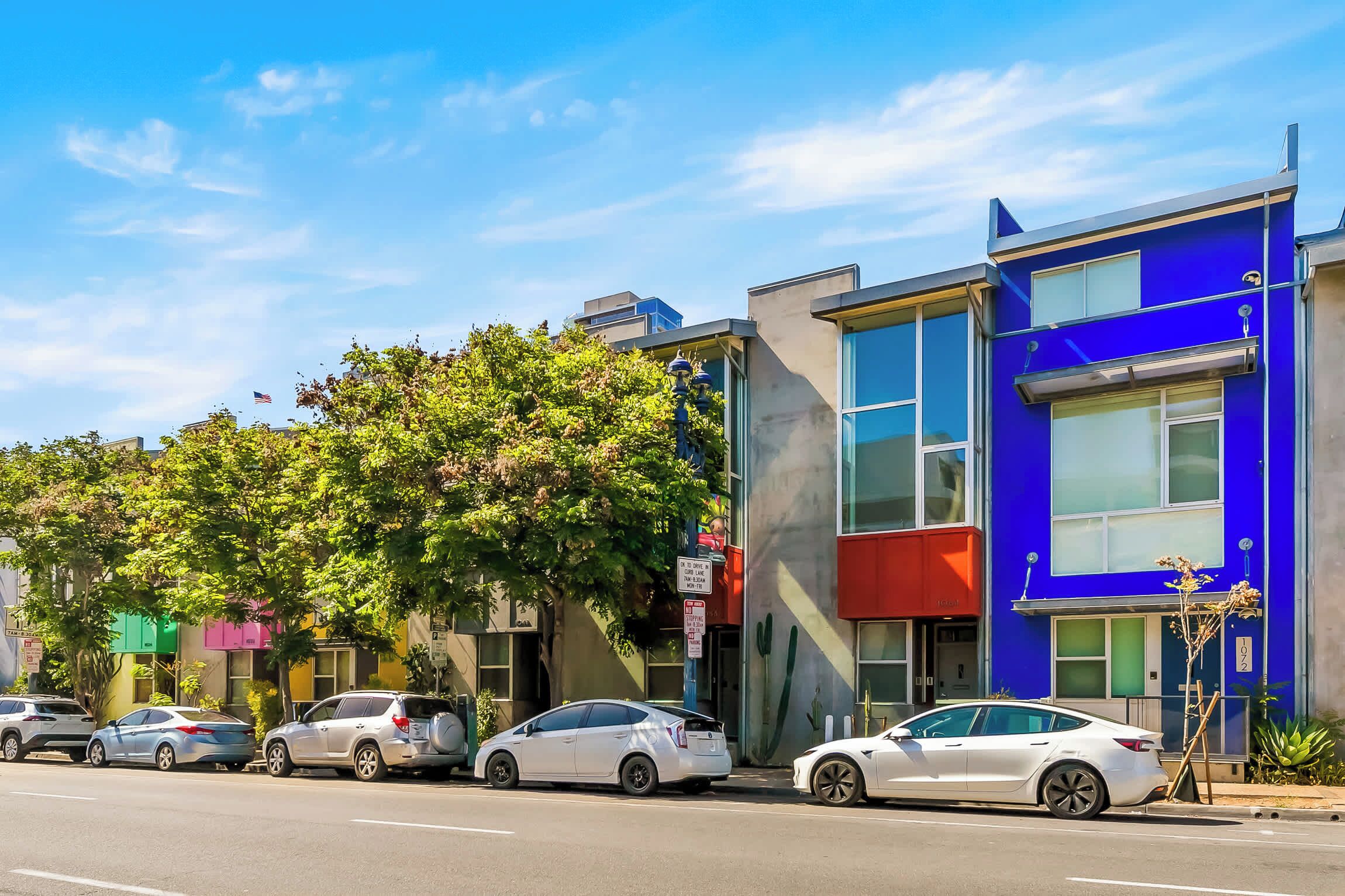 A street view with modern buildings, parked cars, and a clear sky.