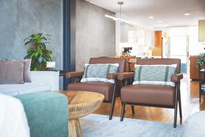 A modern living room with a sofa, two brown leather chairs, a round wooden coffee table, and a potted plant.